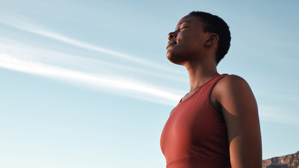 A calm woman stands outdoors with the sky behind her.