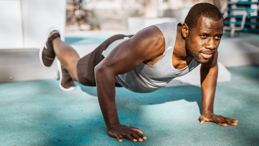 A man does core exercises on the ground outdoors.