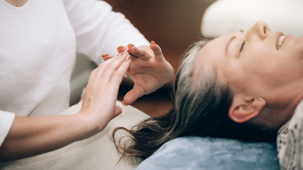 A Reiki healer holds their hands above a woman's head.