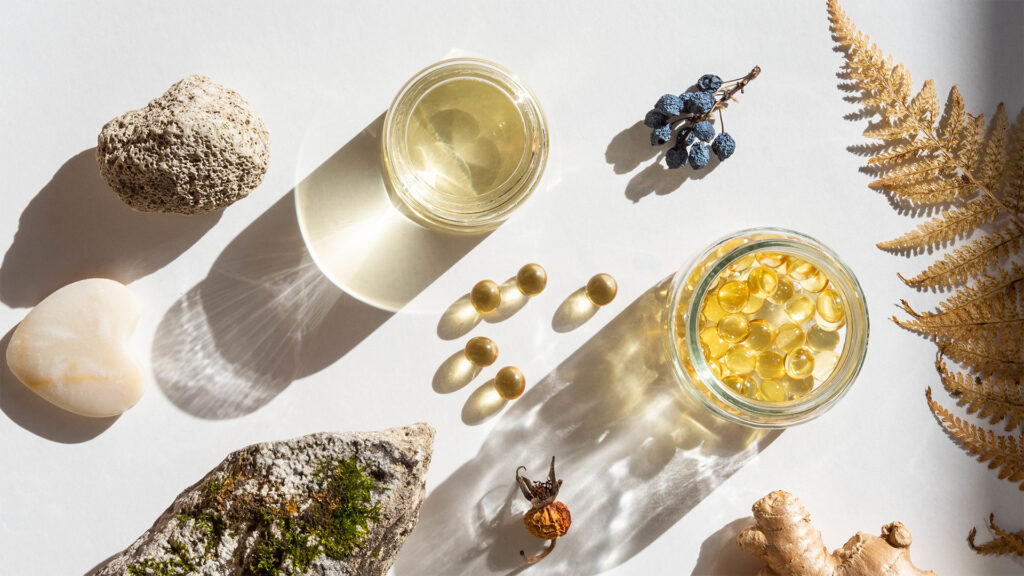 Top-down view of an assortment of supplements, drinks, rocks, and dried plants sitting on a white table.