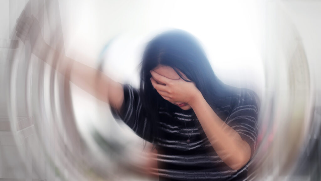 Portrait of a young woman holding her hand to her eyes with the image becoming blurred around her.