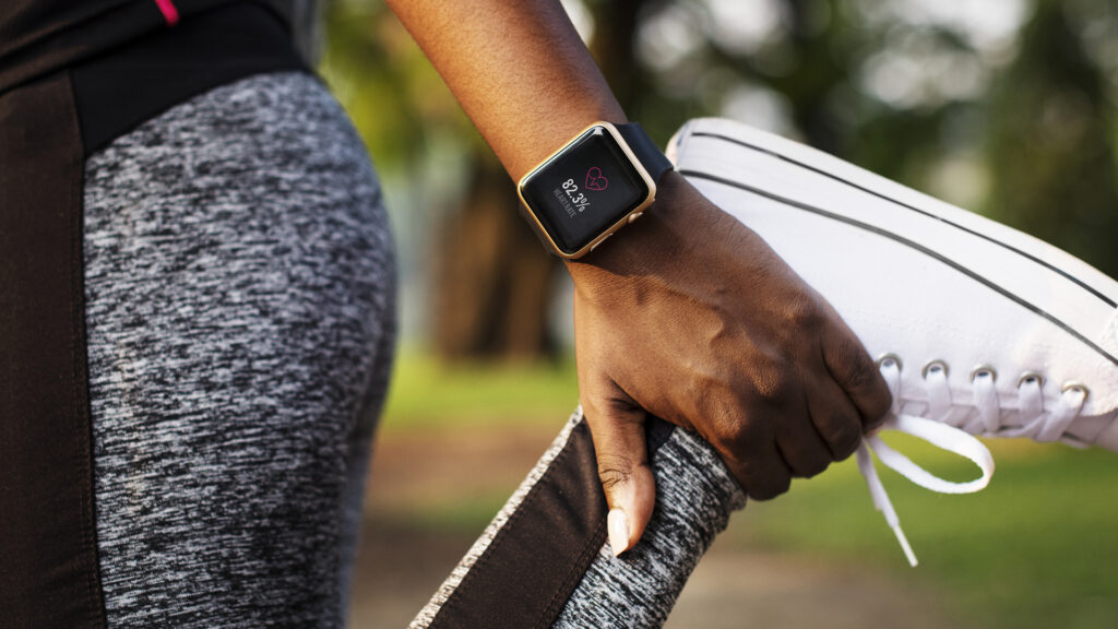 Close-up image of a woman holding her ankle while stretching her legs with a smart watch on her wrist.