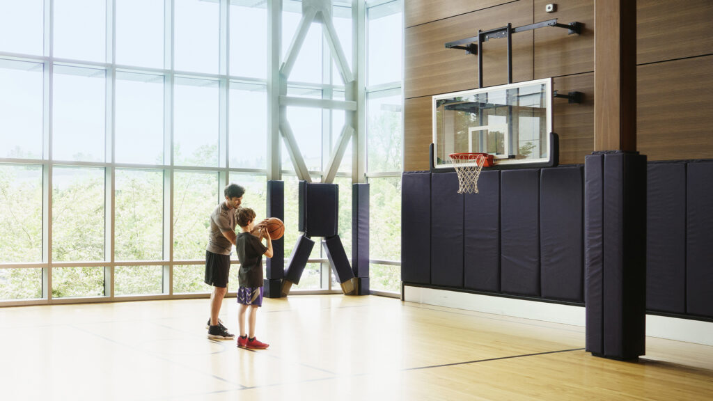 A father is teaching his young son to shoot a basketball in a gym.